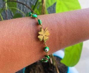 Pulseira Olho Grego Verde com Trevo Dourado A Pulseira Olho Grego Verde com Trevo de Quatro Folhas Dourado reúne dois elementos conhecidos por seu forte significado simbólico em uma peça delicada, moderna e fácil de usar. Ao longo da pulseira estão pequenas contas verdes com o tradicional desenho de olho grego, enquanto o centro da composição recebe um trevo de quatro folhas em tom dourado, criando um ponto de destaque no pulso. A combinação entre verde e dourado deixa a peça visualmente marcante sem exigir um design exagerado. Por isso, pode acompanhar desde looks simples do dia a dia até produções mais elaboradas. Pulseira com olho grego verde O olho grego, também conhecido internacionalmente como evil eye, aparece há séculos em amuletos e objetos ornamentais de diferentes culturas. O Metropolitan Museum of Art possui em sua coleção histórica um amuleto com um motivo semelhante a um olho, associado culturalmente à ideia de afastar o chamado “mau-olhado”. Na moda e nos acessórios contemporâneos, esse símbolo aparece em colares, brincos, pulseiras, pingentes e outros itens decorativos. Nesta pulseira, o motivo aparece em contas verdes, criando uma versão diferente das tradicionais peças com predominância de azul. Conheça um amuleto histórico com motivo de olho no Metropolitan Museum of Art Trevo de quatro folhas dourado O centro da pulseira possui um trevo de quatro folhas, outro elemento amplamente utilizado em joias, semijoias e acessórios. O trevo de quatro folhas é tradicionalmente associado à ideia de sorte, razão pela qual aparece com frequência em pulseiras, colares, pingentes e presentes simbólicos. Essa associação também pode ser encontrada em coleções de joalheria inspiradas no formato do trevo de quatro folhas. Nesta peça, o trevo apresenta acabamento visual dourado, criando contraste com as contas verdes distribuídas ao redor da pulseira. Dois símbolos em uma única pulseira O diferencial deste modelo está na combinação entre olho grego e trevo de quatro folhas. No mercado de acessórios, os dois elementos aparecem inclusive juntos em pulseiras apresentadas como peças simbólicas ou amuletos. Há modelos comercializados especificamente como pulseiras com olho grego e trevo, mostrando que essa é uma combinação já reconhecida na categoria. A pulseira pode ser escolhida simplesmente por sua aparência ou pelo significado cultural associado aos símbolos. Não há necessidade de atribuir qualquer efeito real de proteção ou sorte à peça: esses significados fazem parte da tradição e do simbolismo popular dos elementos presentes no acessório. Verde e dourado em uma combinação marcante A combinação entre verde e dourado é um dos principais destaques visuais desta pulseira. O verde das contas cria contraste com o tom metálico do trevo e dos pequenos componentes de ligação da peça. Essa combinação permite utilizar a pulseira com diferentes cores de roupa, especialmente: Branco; Preto; Bege; Marrom; Verde; Tons terrosos; Dourado; Looks neutros; Produções casuais; Looks mais elaborados. Também é possível combinar a pulseira com brincos, anéis ou colares em tons dourados. Use sozinha ou crie um mix de pulseiras A Pulseira Olho Grego Verde com Trevo Dourado pode ser utilizada sozinha para manter o trevo como principal destaque do pulso. Outra possibilidade é combiná-la com outras pulseiras mais finas ou lisas, criando um mix. Ela pode ficar especialmente interessante ao lado de: Pulseiras douradas; Correntes delicadas; Pulseiras de elos; Braceletes finos; Relógios; Outras pulseiras com pequenos pingentes. A escolha depende do estilo desejado. Para uma composição minimalista, use apenas esta pulseira. Para um visual mais marcante, combine diferentes modelos no mesmo pulso. Acessório para diferentes momentos Apesar dos elementos simbólicos, a pulseira não precisa ficar reservada para uma ocasião específica. Ela pode acompanhar diversos momentos do dia, como trabalho, passeios, encontros, viagens, aniversários, confraternizações e outras ocasiões. O design com pequenas contas e um elemento central torna a peça fácil de incluir em diferentes produções. Também pode complementar looks de verão, peças em tons naturais ou roupas mais básicas que precisam de um pequeno ponto de cor. Pulseira para presentear A combinação entre olho grego e trevo também torna este modelo uma opção interessante de presente. A pulseira pode ser escolhida para aniversários, amigo secreto, datas comemorativas ou simplesmente como um pequeno presente para alguém especial. É especialmente adequada para pessoas que gostam de: Olho grego; Trevo de quatro folhas; Acessórios verdes; Acessórios dourados; Pulseiras delicadas; Símbolos de sorte; Amuletos decorativos; Peças diferentes para o dia a dia. O simbolismo dos elementos pode acrescentar um significado especial ao presente sem deixar de lado a função principal da peça como acessório. Significado cultural do olho grego A associação do formato de olho com amuletos possui uma história bastante antiga. Além do Metropolitan Museum of Art, o British Museum mantém peças históricas descritas como amuletos relacionados ao chamado “olho da inveja” ou “evil eye”, demonstrando que esse simbolismo apareceu em diferentes épocas e regiões. Hoje, o motivo é encontrado amplamente na moda e pode ser usado independentemente de crenças pessoais, simplesmente como elemento decorativo. Uma pulseira delicada e cheia de detalhes Visualmente, a peça combina pequenos elementos para criar uma composição equilibrada. As contas verdes chamam atenção pela repetição do desenho de olho, enquanto o trevo dourado central quebra a sequência e se transforma no elemento principal. O resultado é uma pulseira que pode chamar atenção pelos detalhes sem precisar utilizar pedras grandes ou pingentes volumosos. É uma alternativa para quem gosta de acessórios com personalidade, mas prefere peças menores e mais delicadas. Produto vendido pela OnCompre A Pulseira Olho Grego Verde com Trevo de Quatro Folhas Dourado é um produto vendido pela própria OnCompre. Além deste modelo, você pode encontrar outros acessórios, pulseiras, colares, relógios, presentes e produtos selecionados disponíveis no marketplace. Conheça outros produtos disponíveis na OnCompre