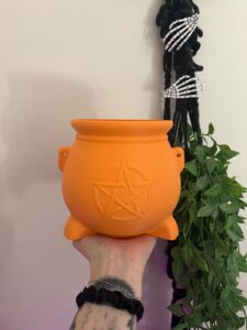 Caldeirão de Bruxa Halloween: um clássico da decoração de terror Bruxa sem caldeirão? A decoração de Halloween não estaria completa. O Caldeirão de Bruxa Halloween traz um dos elementos mais conhecidos do imaginário das bruxas para uma peça decorativa cheia de personalidade. Produzido em impressão 3D, é perfeito para quem deseja criar uma atmosfera de terror, magia e mistério em festas ou na decoração do dia a dia. Decoração perfeita para o Halloween 🎃 O caldeirão de bruxa aparece frequentemente em decorações do Dia das Bruxas ao lado de outros elementos clássicos como fantasmas, caveiras, morcegos e abóboras. Ele combina especialmente com: Decoração de Halloween Festa de Dia das Bruxas Festa de terror Festa à fantasia Cenários temáticos Decoração dark Decoração de bruxa Mesas temáticas Eventos de outubro Noite de filmes de terror O Halloween é celebrado em 31 de outubro e reúne tradições relacionadas a fantasias, elementos sobrenaturais e o famoso “doces ou travessuras”. Você pode conhecer mais sobre a história e as tradições do Halloween na Encyclopaedia Britannica. Caldeirão decorativo para quem ama bruxas O caldeirão decorativo de bruxa também funciona muito bem fora das festas de Halloween. Quem gosta de estética mística, witchy ou alternativa pode incorporar a peça à decoração durante todo o ano. Fica interessante em: Estantes Prateleiras Mesas Nichos Quartos Home office Setup Cantinhos místicos Coleções temáticas É uma peça que chama atenção mesmo quando usada sozinha. Estética witchy, mística e sombria Caldeirões fazem parte do imaginário popular ligado às bruxas, poções e histórias de fantasia. Por isso, essa peça combina com diferentes estilos de decoração: Witchy Dark Gótica Mística Fantasy Halloween Terror Medieval fantástica Ocultista decorativa Você pode combiná-la com velas decorativas, livros, caveiras, fantasmas, luas e outros elementos para criar um ambiente ainda mais temático. Monte um cantinho de terror Se você gosta de decoração de horror, o Caldeirão de Bruxa pode ser o ponto de partida para montar uma composição completa. Experimente combinar com: Esqueletos Fantasmas Caveiras Morcegos Aranhas decorativas Teias falsas Abóboras Velas Miniaturas de terror Luzes temáticas Assim, uma simples prateleira pode ganhar aparência de cenário de Halloween. Para fãs de terror e fantasia O Caldeirão de Bruxa Halloween também é uma opção diferente para presentear. Pode agradar especialmente: Fãs de filmes de terror Pessoas que amam Halloween Fãs de bruxas Colecionadores Pessoas que gostam de decoração gótica Fãs de fantasia Quem gosta de estética witchy Fãs de impressão 3D Pessoas que colecionam itens temáticos Por que escolher o Caldeirão de Bruxa Halloween? Design inspirado em caldeirão de bruxa Ideal para decoração de Halloween Perfeito para festas de terror Produzido em impressão 3D Combina com decoração dark e gótica Ótimo para cenários temáticos Pode decorar estantes e prateleiras Ideal para fãs de bruxas e fantasia Excelente opção para presente Pode ser usado durante todo o ano Conheça outros produtos da Casa&decor 3D O Caldeirão de Bruxa Halloween é um produto da Casa&decor 3D. Conheça também os outros produtos da Casa&decor 3D disponíveis na OnCompre e encontre fantasmas, esqueletos, miniaturas e outras peças para montar uma decoração criativa e cheia de personalidade. Aproveite a promoção Preço normal: R$ 103,00 🎃 Preço promocional: R$ 85,00 Você economiza R$ 18,00. Garanta seu Caldeirão de Bruxa Halloween e transforme seu cantinho em um cenário digno de uma noite de terror.